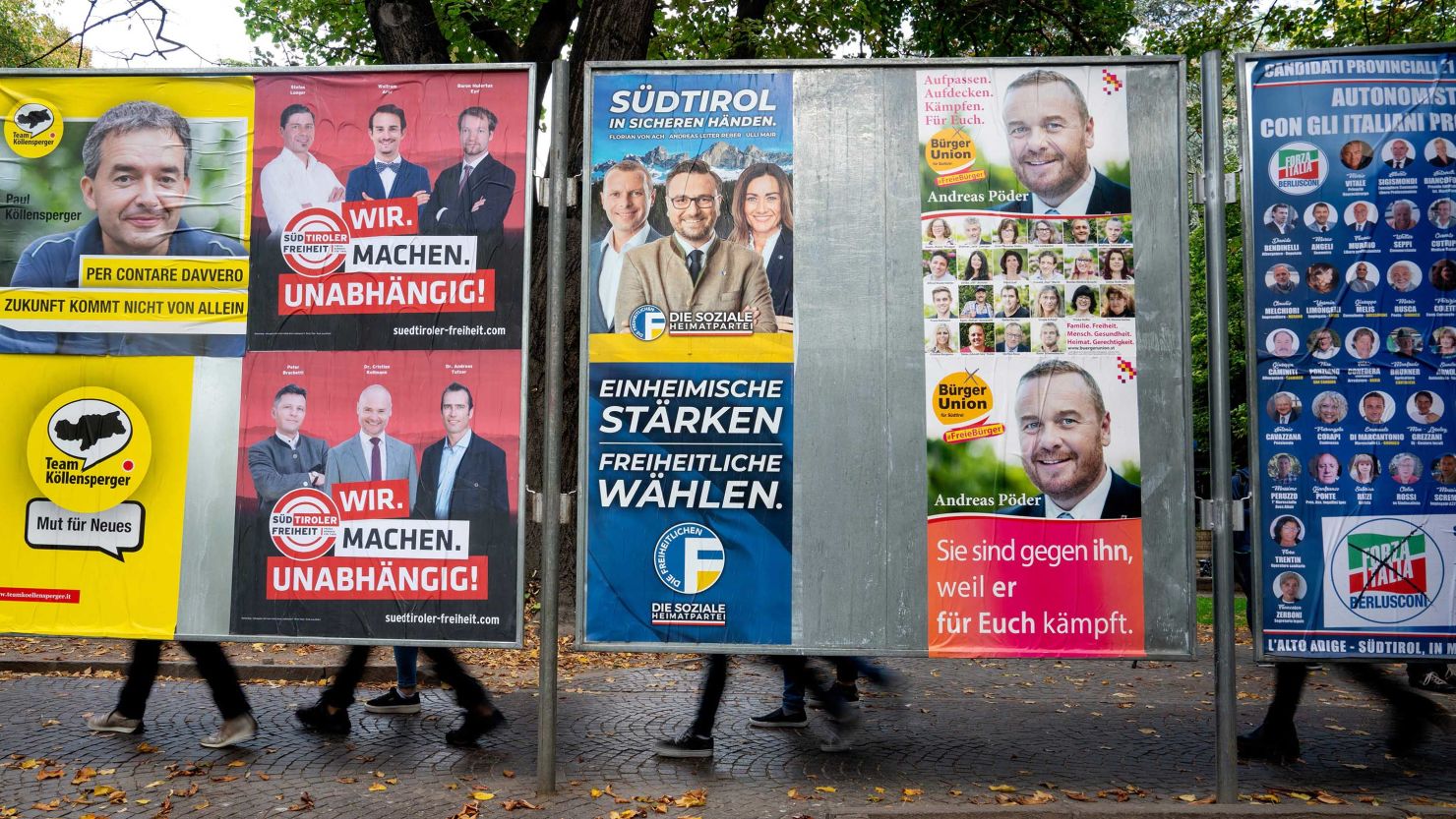 People pass behind election posters in Bolzano, Italy on October 15, 2018.