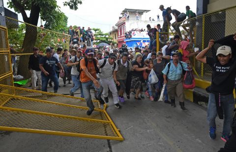 Honduran migrants heading in a caravan to the United States rush through the Guatemala-Mexico border bridge after tearing down its gate in Ciudad Hidalgo, Mexico, on Friday, October 19. 
