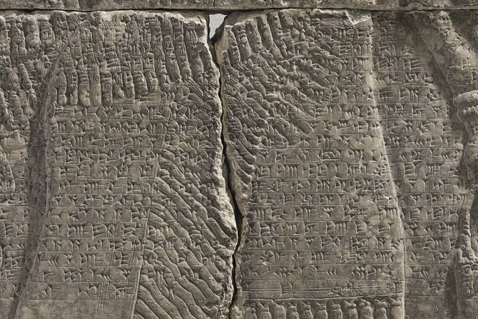 A band of text written in cuneiform -- one of the earliest systems of writing -- runs across the center of the panel. 