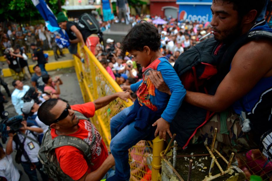 A child is lifted over the border fence as thousands of Honduran migrants rush across the border toward Mexico, in Tecun Uman, Guatemala, Friday, October 19. 