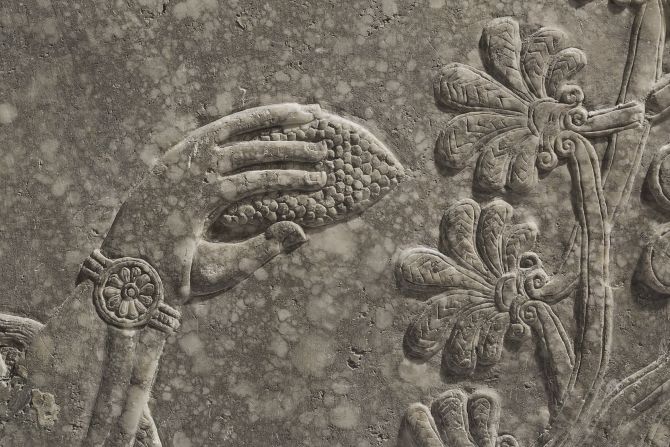 With his right hand, he anoints a stylized palm tree with a pine cone. 