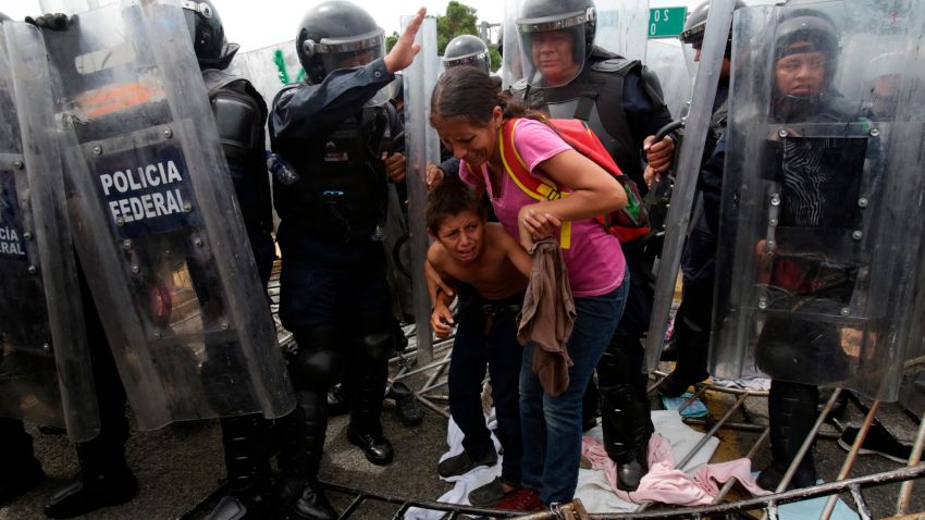 A Honduran migrant mother and child cower in fear as they are surrounded by Mexican Federal Police in riot gear, at the border crossing in Ciudad Hidalgo, Mexico, Friday, Oct. 19, 2018. Central Americans traveling in a mass caravan broke through a Guatemalan border fence and streamed by the thousands toward Mexican territory, defying Mexican authorities' entreaties for an orderly migration and U.S. President Donald Trump's threats of retaliation. 