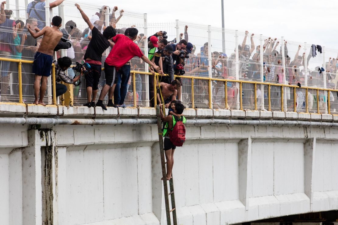 A man helps three-year-old Carlitos off the bridge and be lowered down to his mother, waiting on a raft on the river below.