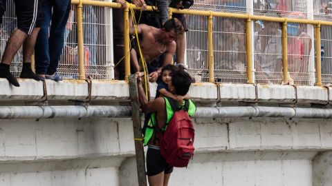 A man helps three-year-old Carlitos off the bridge and be lowered down to his mother, waiting on a raft on the river below.