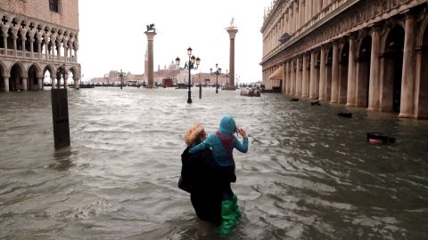 A woman holds a child as she walks in a flooded Saint Mark Square.