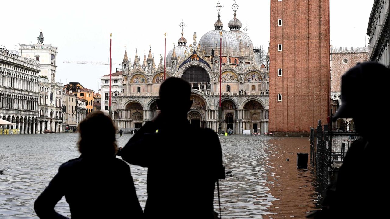 Tourists take pictures in the flooded St Mark's Square during a high-water alert in Venice on October 29, 2018.