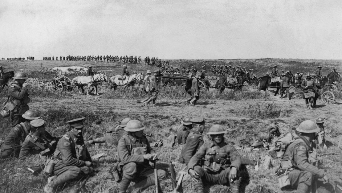 1917: Canadian troops sit and take a break in a field during a pause in their attack on the Cambrai front, France, Western Front. In the background artillery is moved by soldiers with horses.