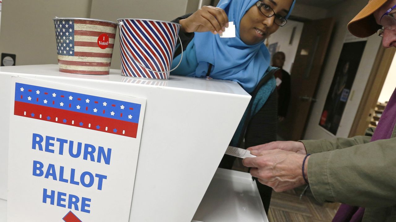An election judge, left, has an "I VOTED" sticker ready to hand to a voter after he inserts his ballot into the machine as people took advantage of early voting Thursday, Oct. 18, 2018, in Minneapolis. (AP Photo/Jim Mone)