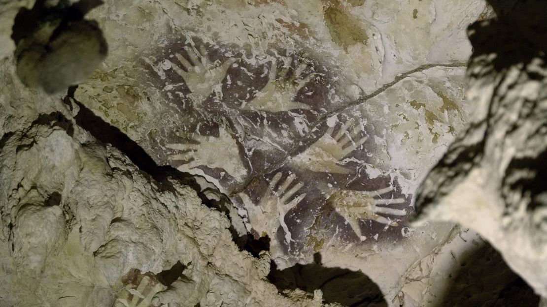 Composition of mulberry-colored hand stencils superimposed over older reddish/orange hand stencils. The two styles are separated by at least 20,000 years.