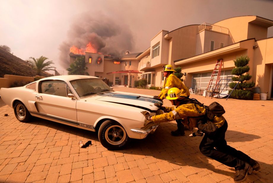 Firefighters push a vehicle from a garage as the Woolsey Fire burns a home in Malibu on November 9.