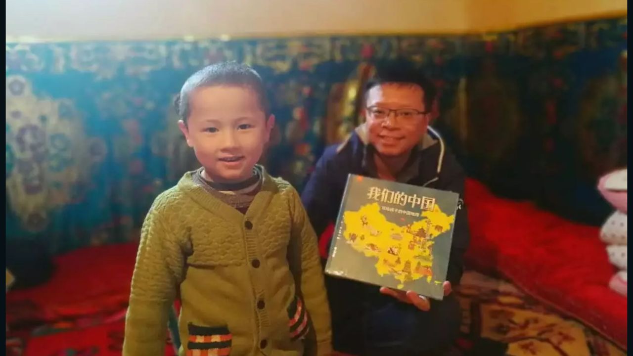 A civilian worker presents a Uyghur child whom he has been assigned to treat as his "relative" with a picture book titled Our China, in an undated photo from Xinjiang's Chinese Communist Youth League.