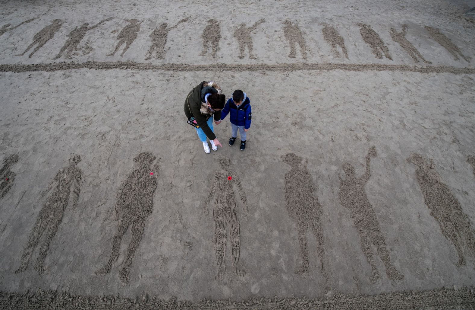 A woman and her son look at etchings in the sand created by the public as members of the public gather on Sunny Sands Beach in Folkstone, England on Sunday. 