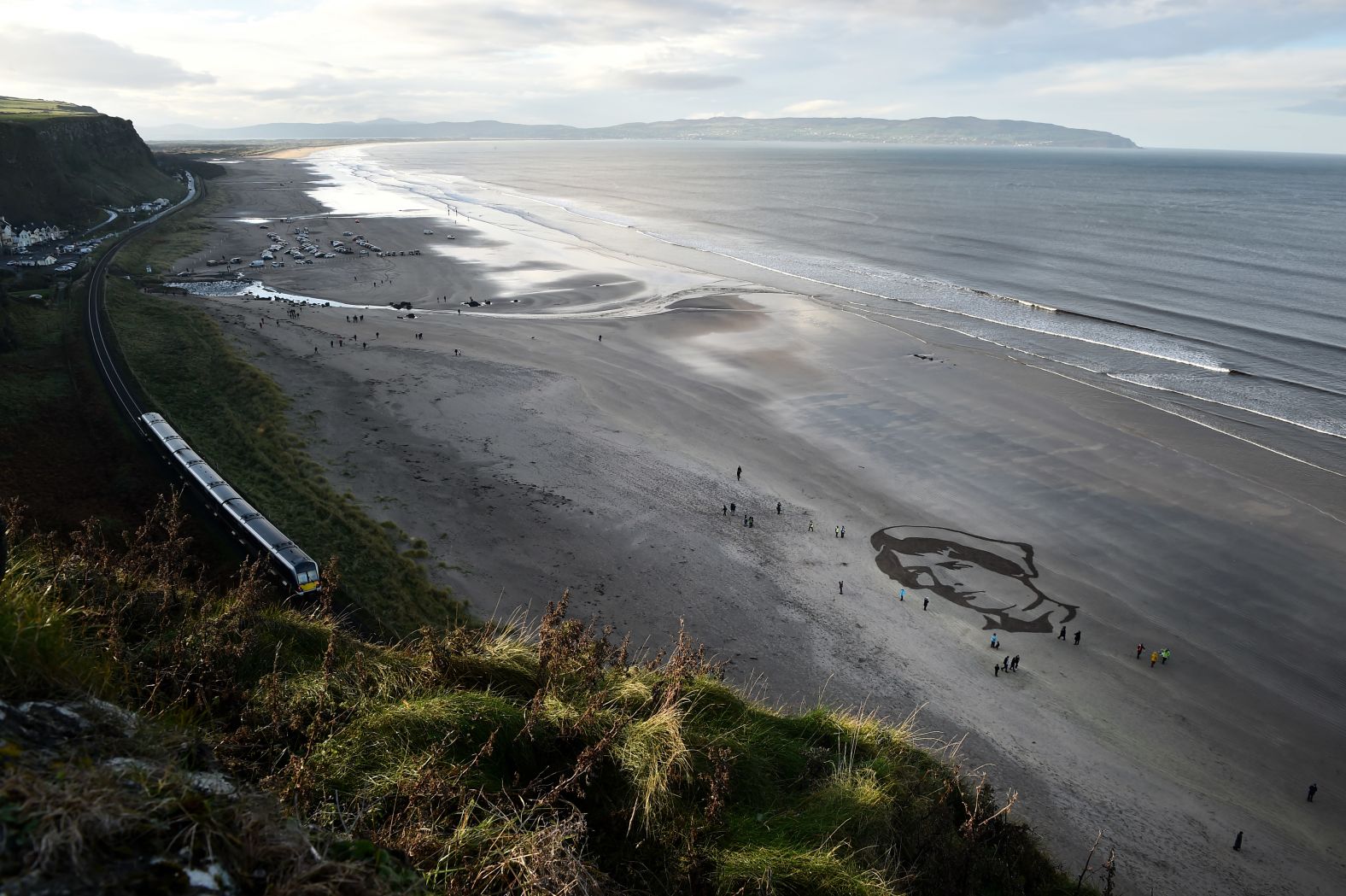 Members of the public gather Sunday around a portrait drawn in the sand of British Army Staff Nurse Rachel Ferguson on Downhill beach as part of the "Pages of the Sea" public art project curated by filmmaker Danny Boyle.