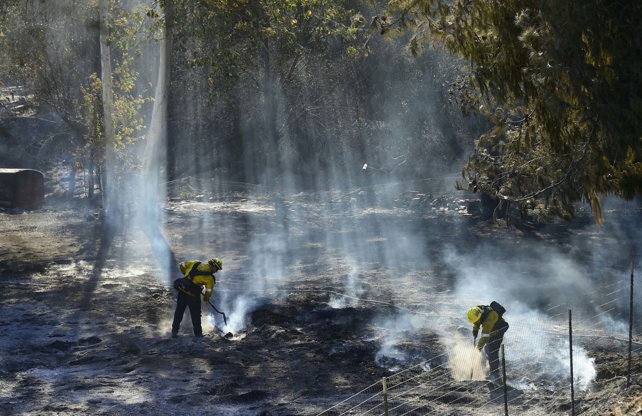 Firefighters douse embers off a canyon road that cuts across the mountains to Malibu.