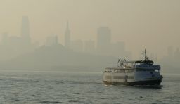 A ferry boat makes its way toward Alcatraz Island as the San Francisco skyline in is obscured by wildfire smoke and haze.