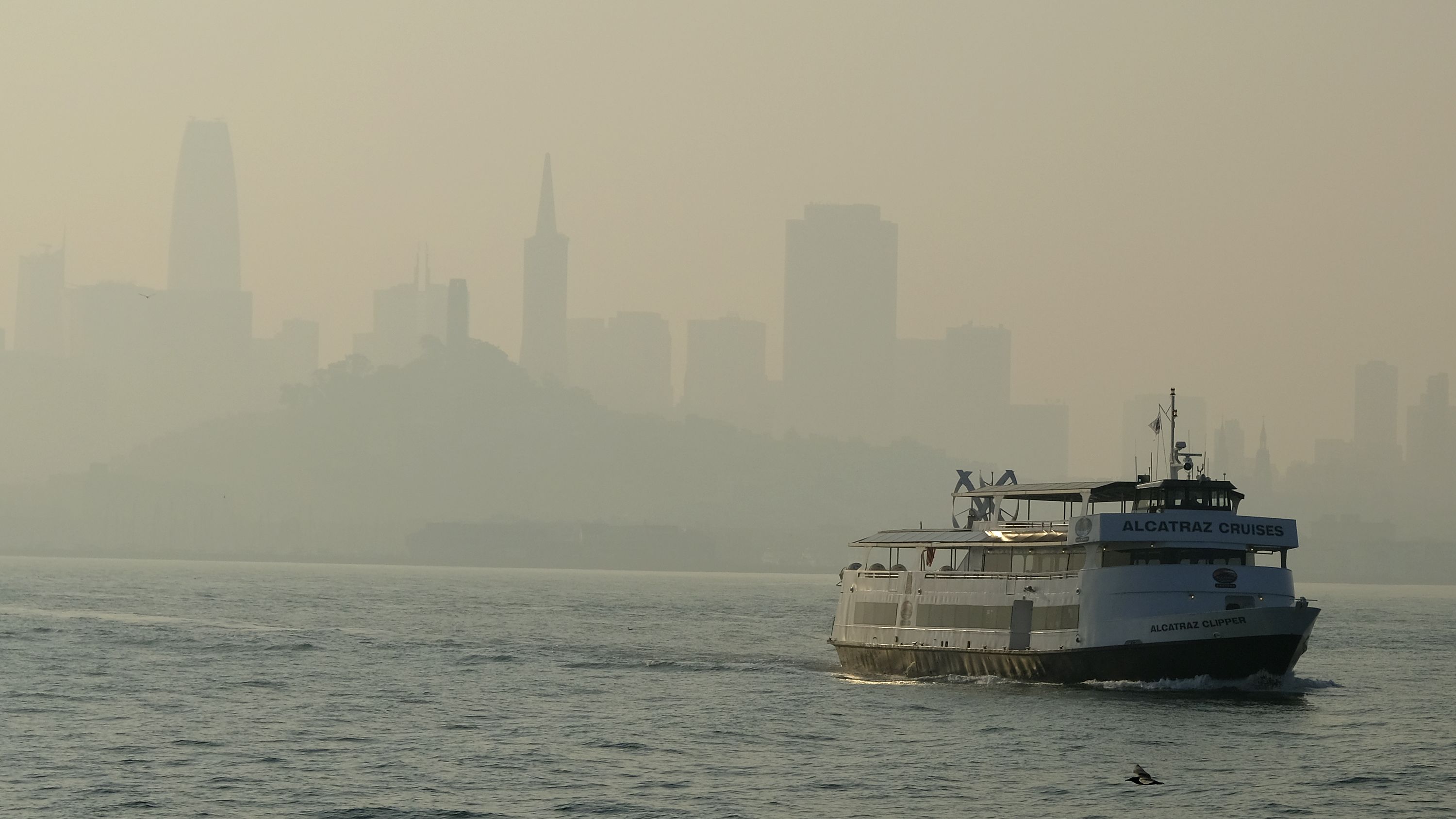 A ferry boat makes its way toward Alcatraz Island as the San Francisco skyline in is obscured by wildfire smoke and haze.
