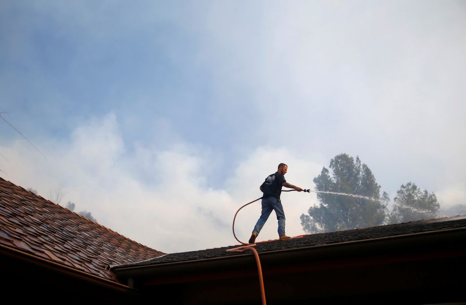 A resident sprays down a roof as firefighters battle the Peak Fire in Simi Valley.