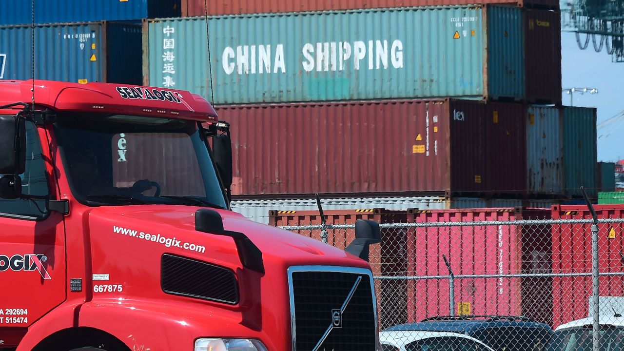 A container delivery truck drives past stacked piles of shipping containers at the Port of Long Beach.