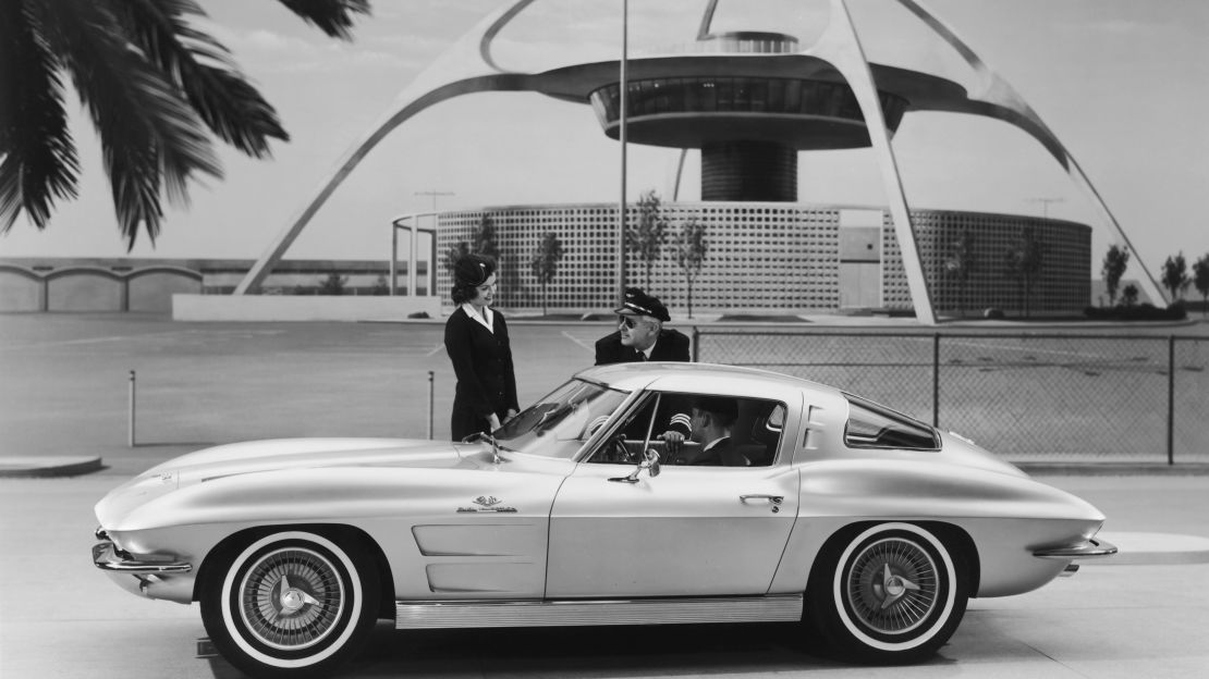 An airplane pilot and a flight attendant greeting the driver of a 1963 Corvette Sting Ray Sport Coupe.