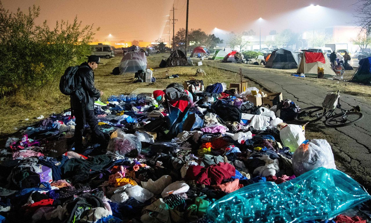 A wildfire evacuee sifts through a pile of clothing at a tent city in a Walmart parking lot in Chico, California, on Saturday, November 17.