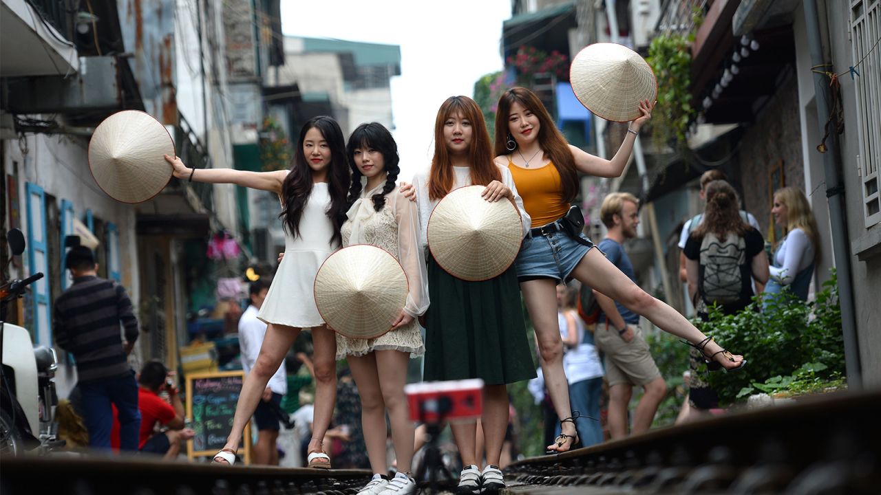 A group of tourists pose with traditional Vietnamese hats on the train tracks.