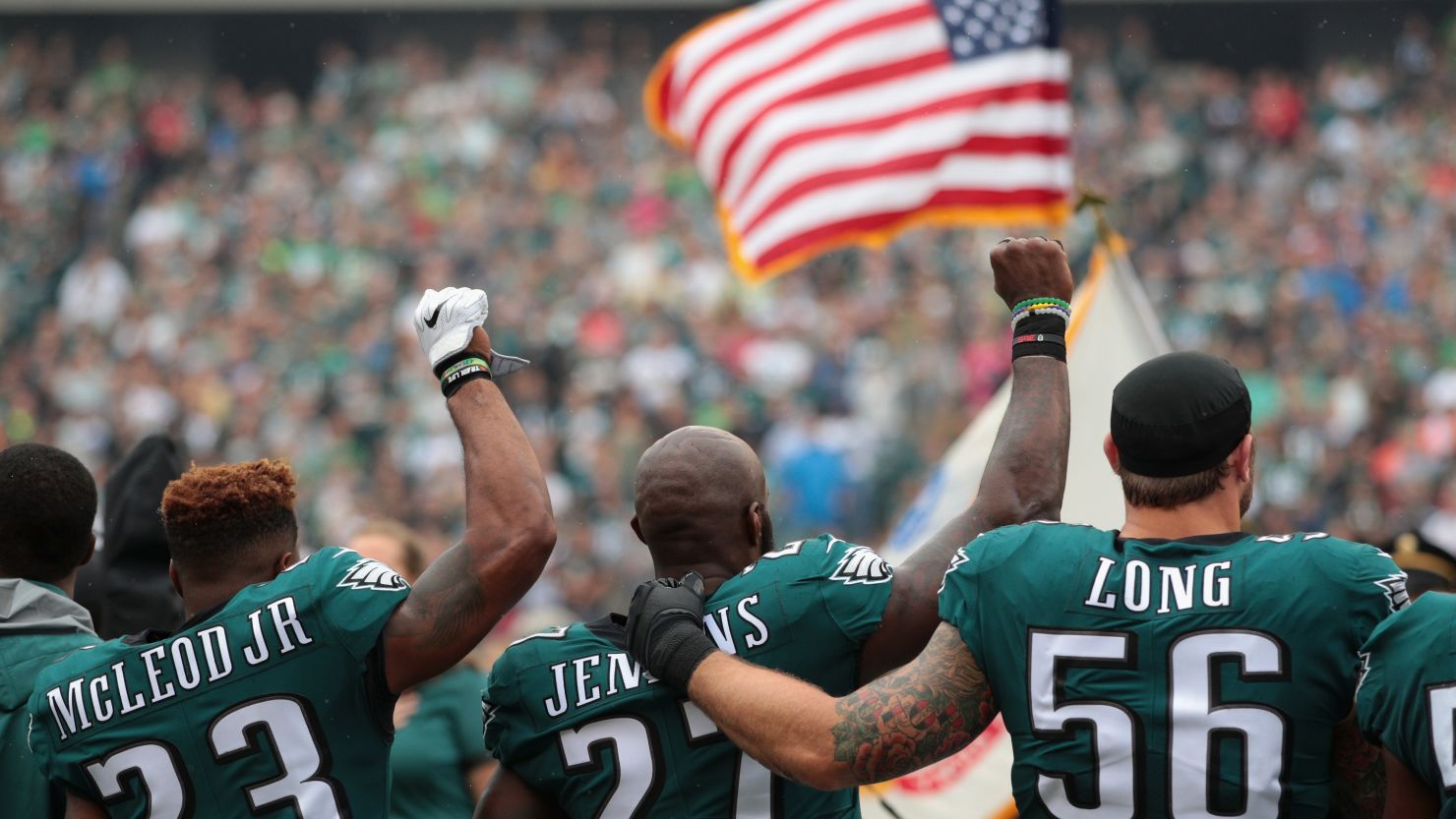 Chris Long (#56) shows solidarity with Philadelphia Eagles teammates Malcolm Jenkins (#27) and Rodney McLeod (#23) during the playing of the US national anthem on October 8, 2017 in Philadelphia. Two weeks earlier, President Donald Trump used a profanity to criticize protesting NFL players. 