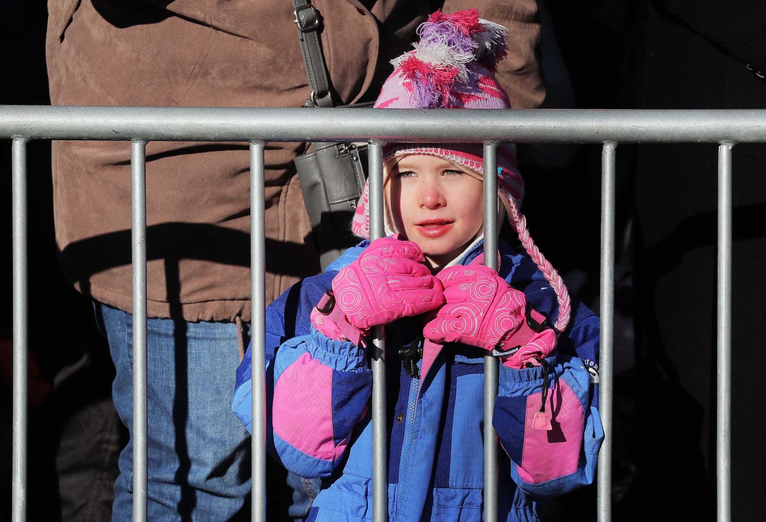 A child watches floats from behind a barricade.
