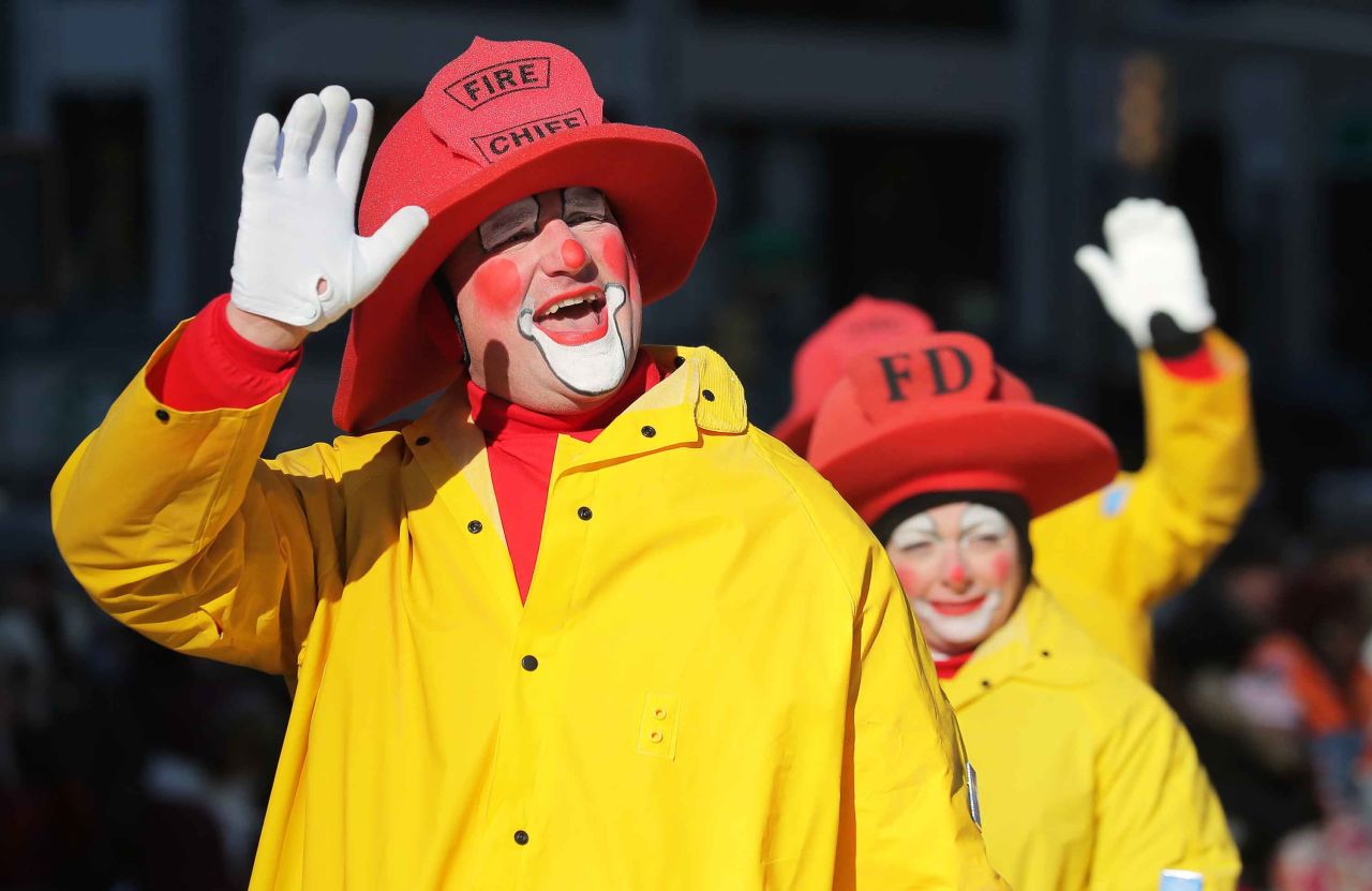 Clowns dressed as firefighters wave to spectators.