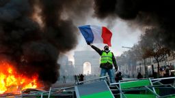 A demonstrator waves the French flag onto a burning barricade on the Champs-Elysees avenue with the Arc de Triomphe in background, during a demonstration against the rising of the fuel taxes, Saturday, Nov. 24, 2018 in Paris. French police fired tear gas and water cannons to disperse demonstrators in Paris Saturday, as thousands gathered in the capital and staged road blockades across the nation to vent anger against rising fuel taxes and Emmanuel Macron's presidency.(AP Photo/Michel Euler)