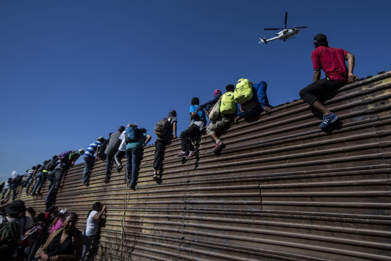 Migrants climb a metal barrier on the border.