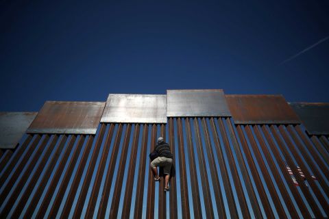 A migrant climbs the fence between Mexico and the United States.