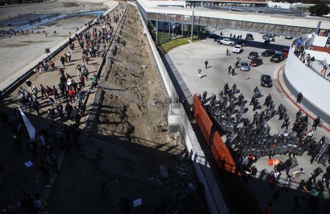 Mexican police, right, stand guard as migrants walk on a bank of the nearly dry Tijuana River. The migrants were making their way toward the El Chaparral port of entry after circumventing a police blockade.