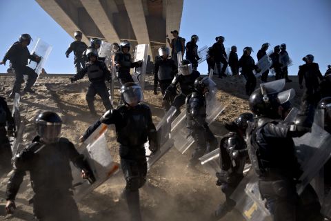 Mexican police run as they try to keep migrants from getting past the border crossing in Tijuana.