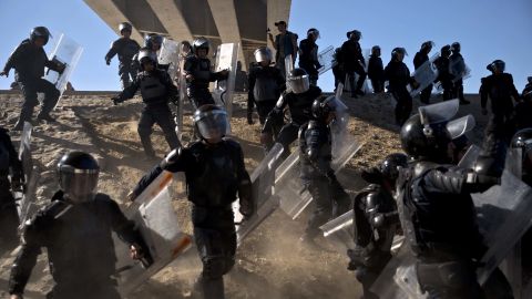 Mexican police run as they try to keep migrants from getting past the Chaparral border crossing in Tijuana, Mexico, on Sunday, 