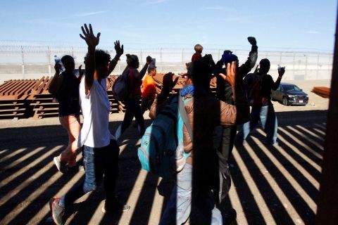 Migrants hold up their hands as US Border Patrol officers detain them. They had jumped over the border fence between Mexico and the United States.