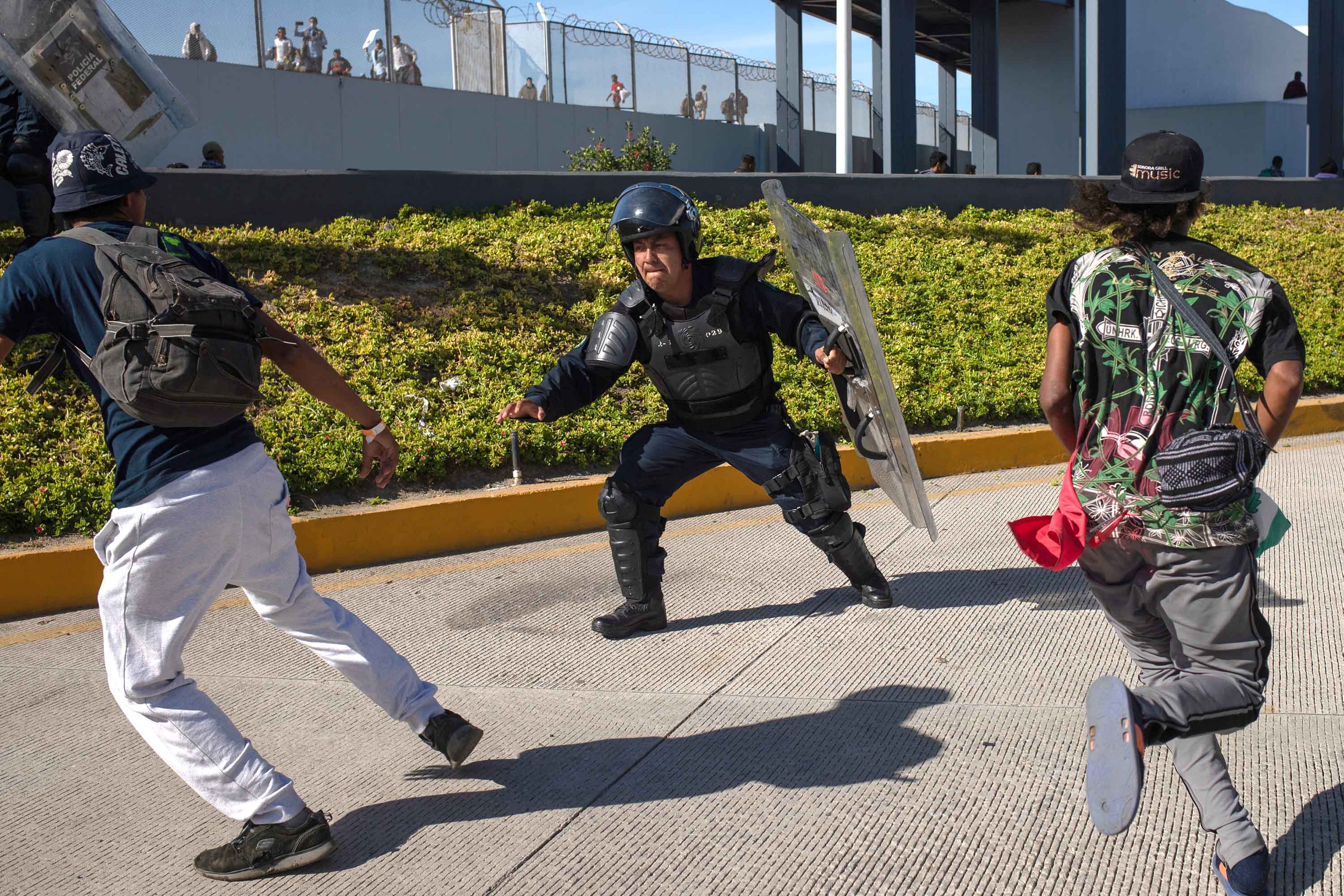 A member of Mexico's Federal Police tries to grab migrants as they attempt to cross the border into the United States on Sunday, November 25.