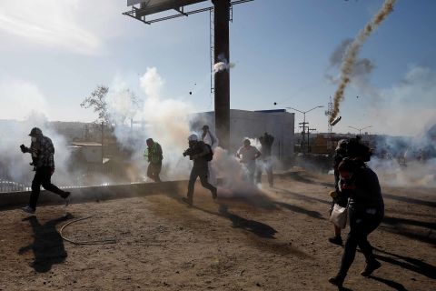 Migrants and journalists run away from tear gas.