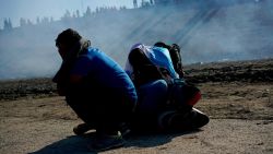 Three Honduran migrants huddle in the riverbank amid tear gas fired by U.S. agents on the Mexico-U.S. border after they and a group of migrants got past Mexican police at the Chaparral border crossing in Tijuana, Mexico, Sunday, Nov. 25, 2018. The mayor of Tijuana has declared a humanitarian crisis in his border city and says that he has asked the United Nations for aid to deal with the approximately 5,000 Central American migrants who have arrived in the city. (AP Photo/Ramon Espinosa)