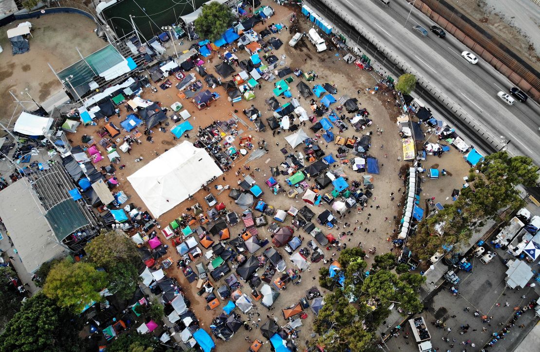 An aerial view of the temporary shelter set up for migrants in Tijuana, with a section of the U.S.-Mexico border barrier visible.