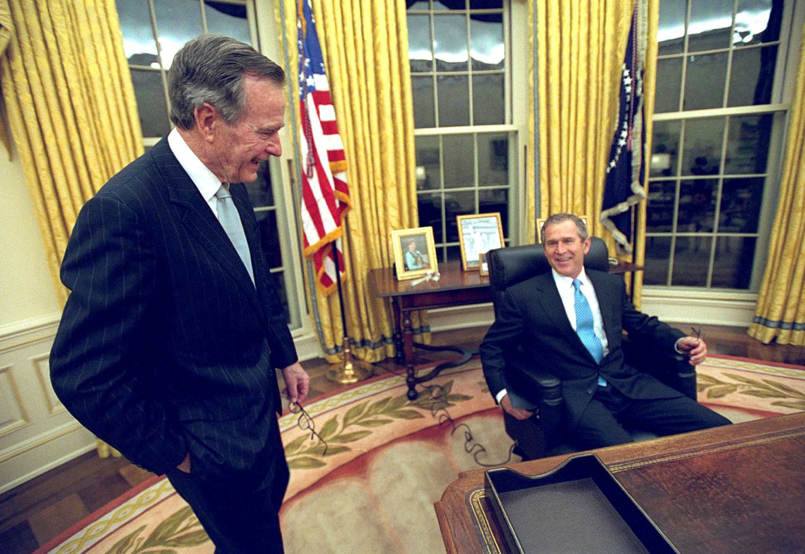 With his father by his side, President George W. Bush sits at his desk in the Oval Office for the first time on Inauguration Day, January 20, 2001.