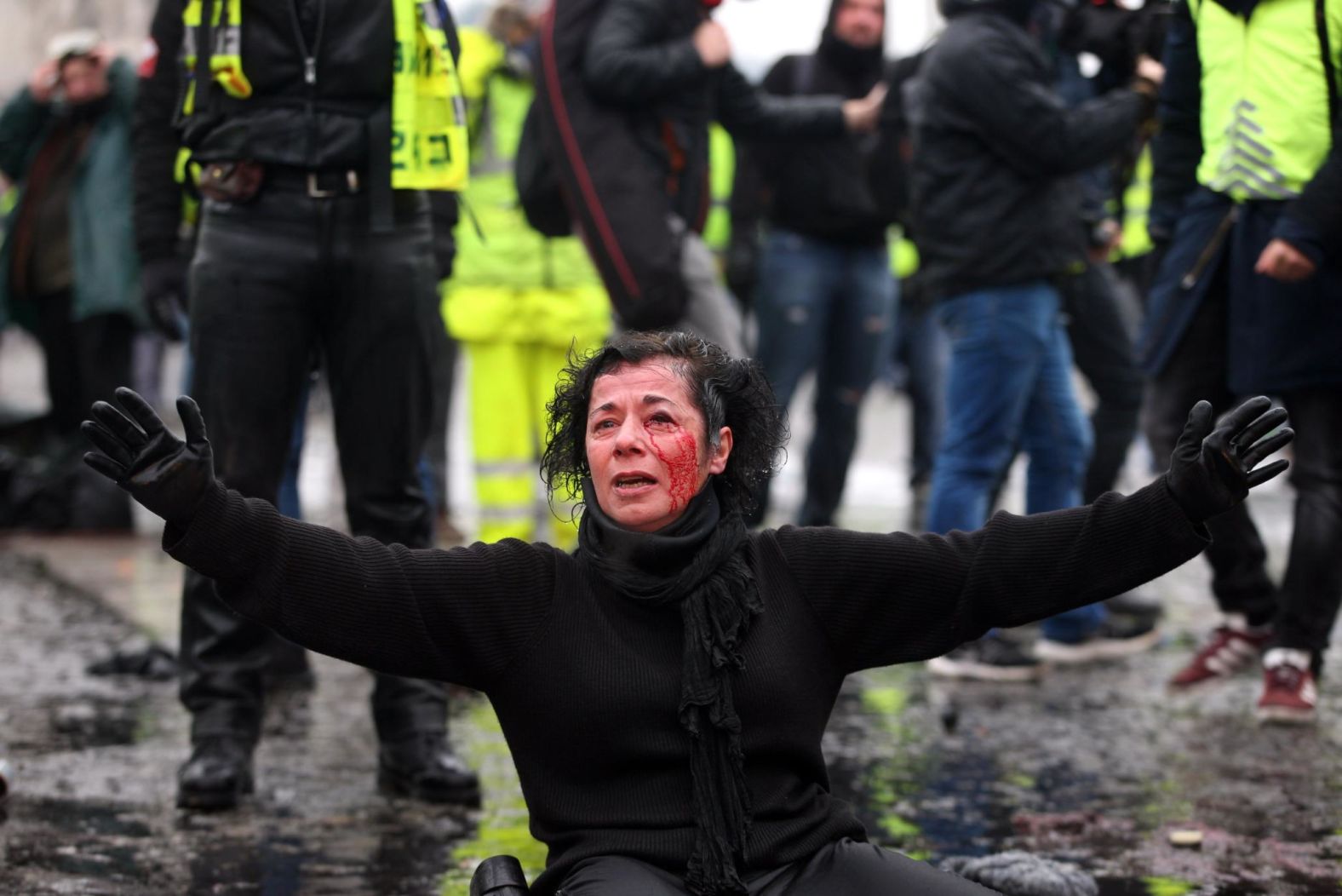 An injured woman sits on the ground as police officers spray yellow vest protesters with tear gas during a protest in Paris on December 1.