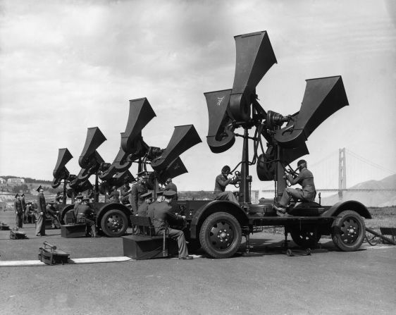 US military personnel operating airplane sound detectors as officers sit and monitor the readings, near San Francisco, California, circa 1944. The Golden Gate bridge is visible in the background.  