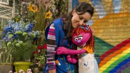 Lily hugs her friend Sofia after painting a rainbow. Lily is a resilient 7-year-old Muppet whose family is staying with friends on Sesame Street after losing their home.