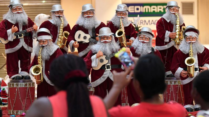 <strong>Kenya:</strong> Shoppers take photos with their mobile phones of musically inclined Santa Claus dolls in Nairobi. The website <a href="index.php?page=&url=https%3A%2F%2Fwww.whychristmas.com%2Fcultures%2Fkenya.shtml" target="_blank" target="_blank">WhyChristmas</a> says "houses and churches are often decorated with colorful balloons, ribbons, paper decorations, flowers and green leaves" during Christmas.