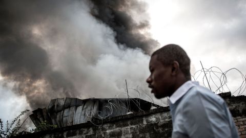 A man walks past smoke rising from the fire.