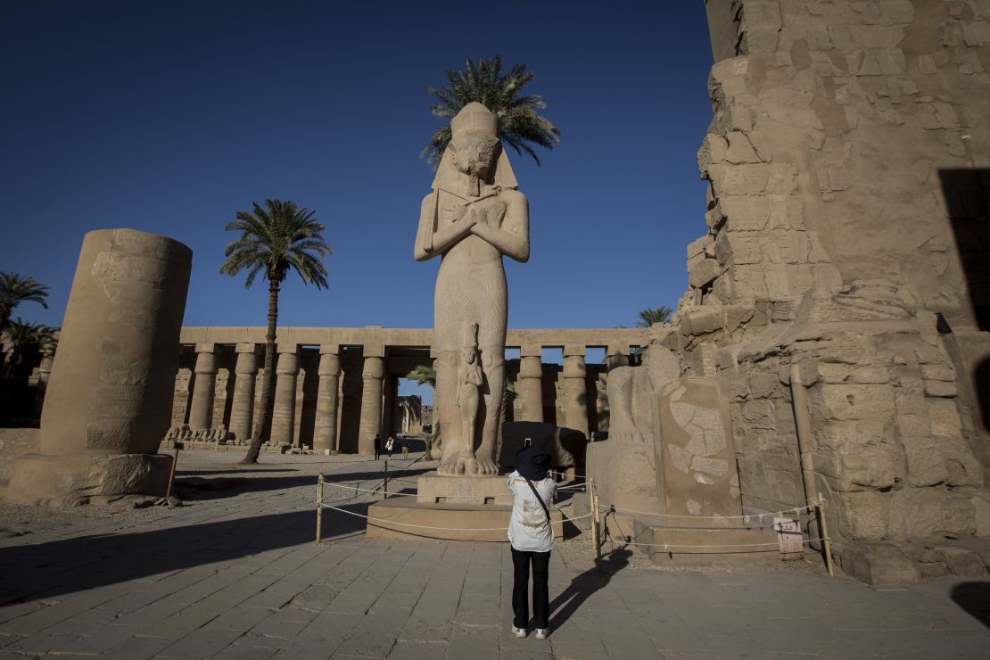 A visitor takes a photo of a Ramses II statue at the entrance of Karnak Temple.