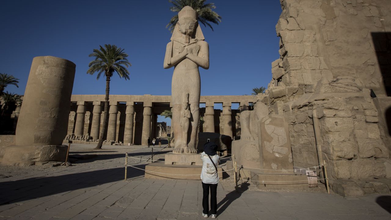 A visitor takes a photo of a Ramses II statue at the entrance of Karnak Temple.