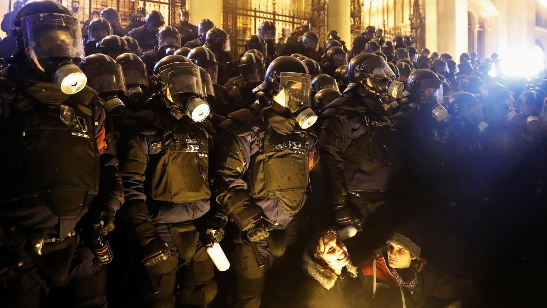 Demonstrators hold position in front of policemen wearing gas masks.