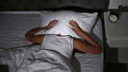 Young woman covering head with pillow in bed at home. Sleep disorder; Shutterstock ID 1163906941; Job: CNNie Design Website