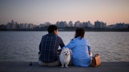 A dog stands between a couple as they sit before the Han river in Seoul on September 20, 2015.  The Han river intersects Seoul from East to West and is lined with parks and walkways making the waterway a popular leisure area throughout the year.  AFP PHOTO / Ed Jones        (Photo credit should read ED JONES/AFP/Getty Images)